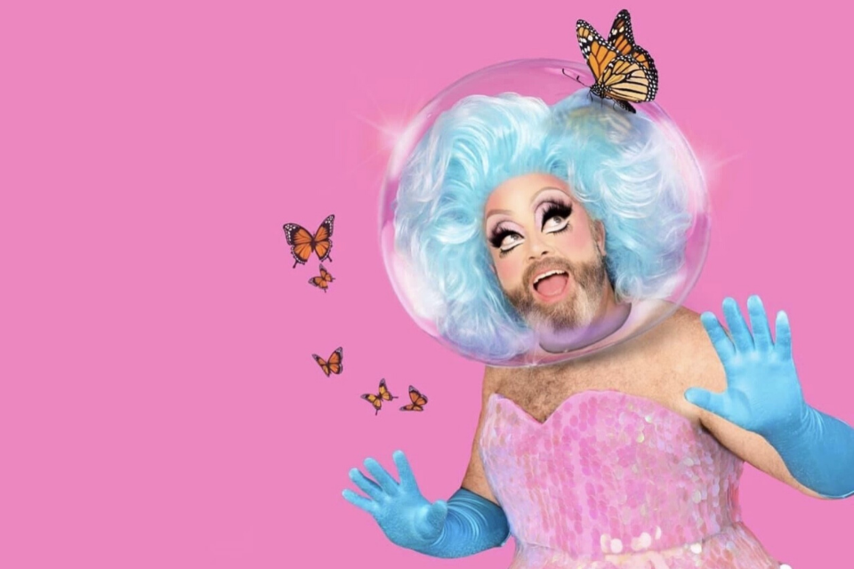 Fay Slift in a sequined pink outfit and blue gloves. Faye's head, with blue hair, is inside a glass bubble with butterflies flying around.