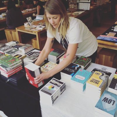 A person stacking books at an Invisible Publishing vendor table