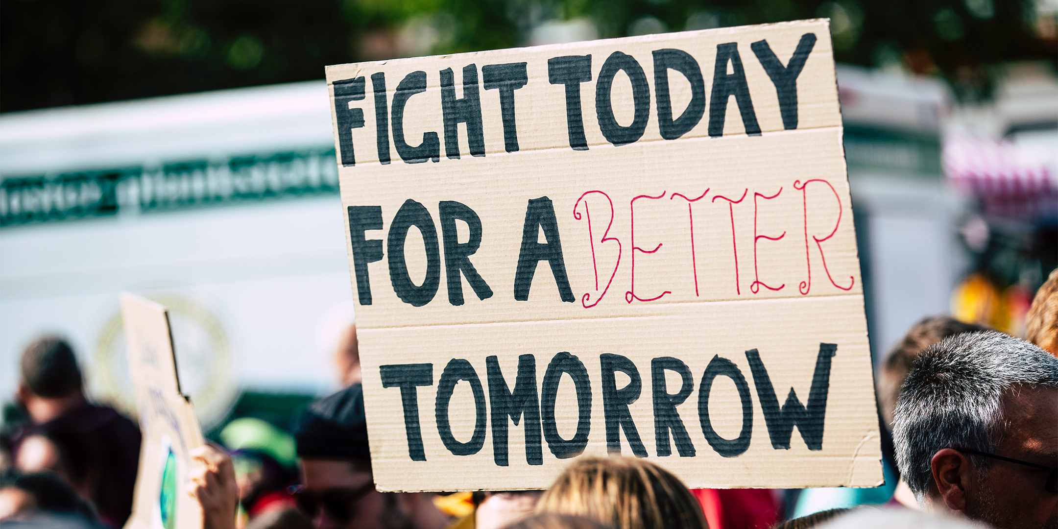 A crowd at a protest with a sign that says "Fight today for a better tomorrow"