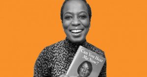 Celina Caesar-Chavannes smiling holding a copy of her new book with a orange background