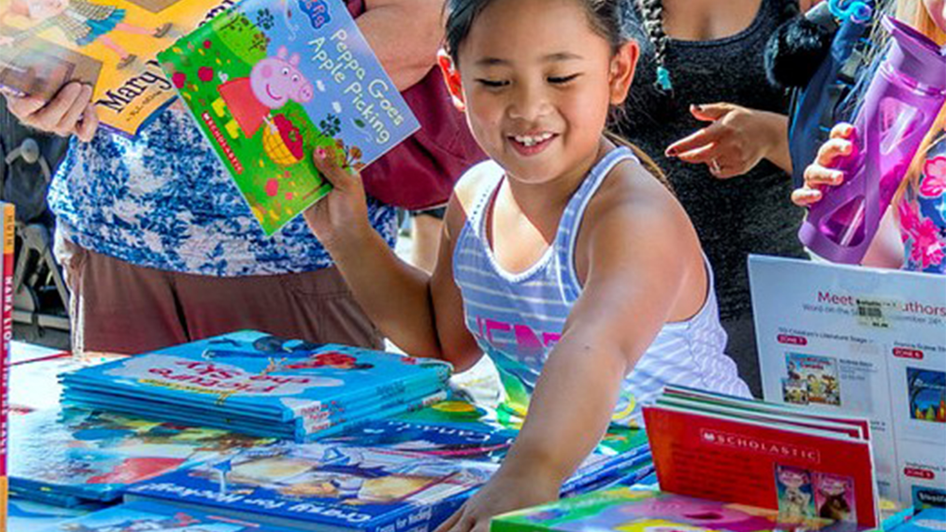A young child at the Word on the Street festival in 2017 browsing books with a smile on their face.