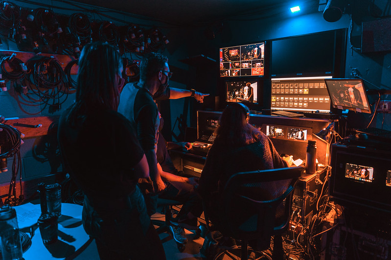 A team of backstage people wearing masks assess video streams on screens