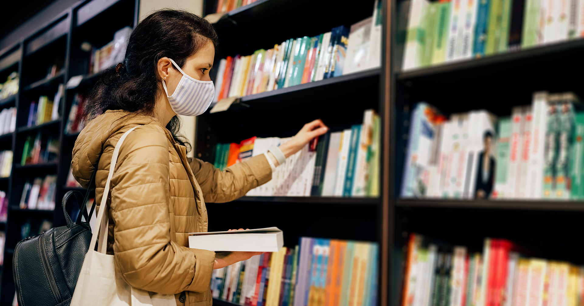 Woman with protective face mask reading a book in the bookstore