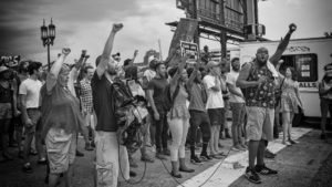People at a Black Lives Matter protest with their arms in the air, holding up a fist.