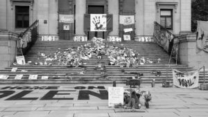 Shoes on a church steps with signs, toys and flowers to protest the treatment of Indigenous peoples and honour the mass graves being uncovered at residential schools.