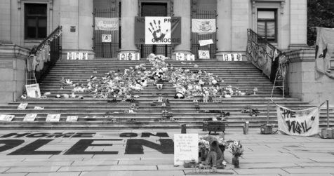 Shoes on a church steps with signs, toys and flowers to protest the treatment of Indigenous peoples and honour the mass graves being uncovered at residential schools.