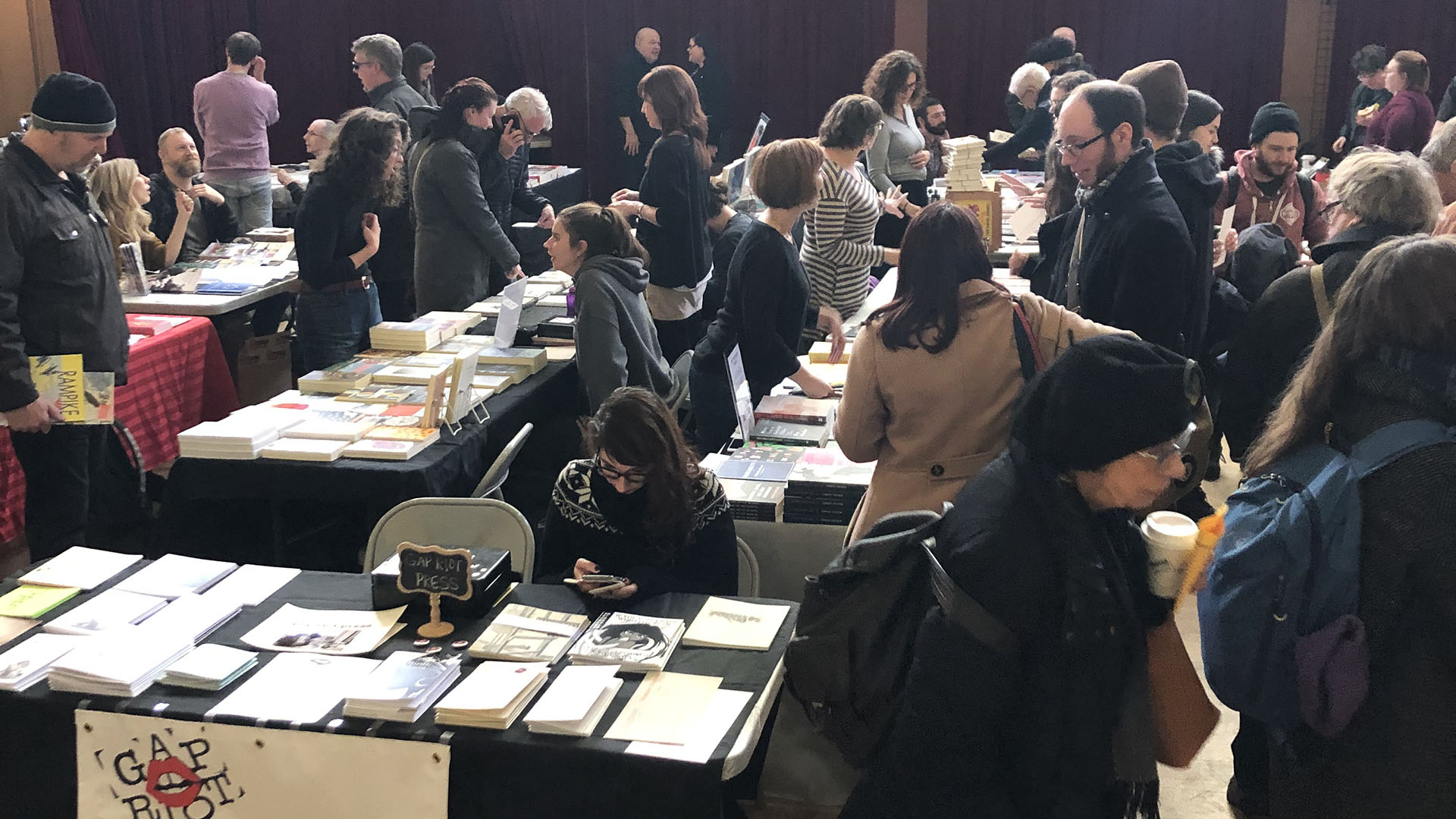 Small Press Market image - features people grouped around different tables from different small presses